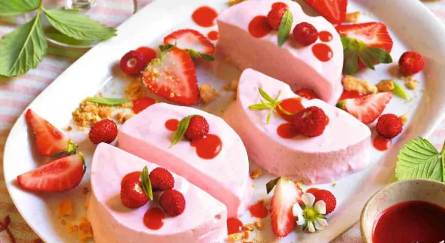 Delizioso semifreddo alle fragole, guarnito con fragoline di bosco, salsa rossa e foglioline verdi.