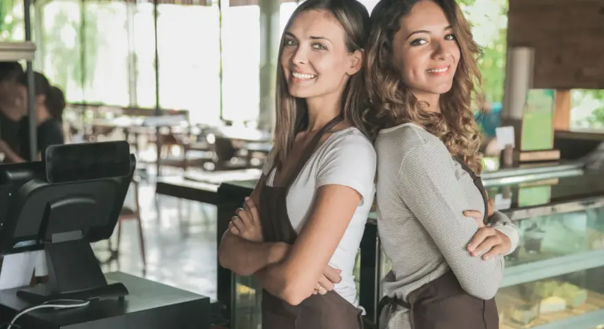 Dwie uśmiechnięte pracownice kawiarni, gotowe do obsługi. Od ilu lat można pracować w gastronomii? Odpowiedź znajdziesz w przepisach.