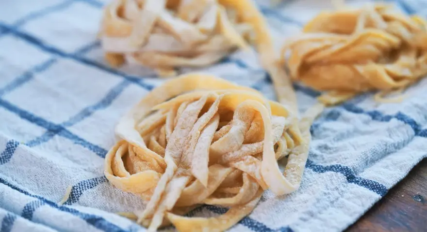Świeże, domowe tagliatelle lub makaron spaghetti ułożone na lnianym ręczniku w kratkę.