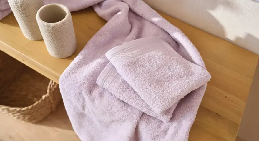 Variedad de tipos de toallas de baño en color lavanda, apiladas sobre una superficie de madera.