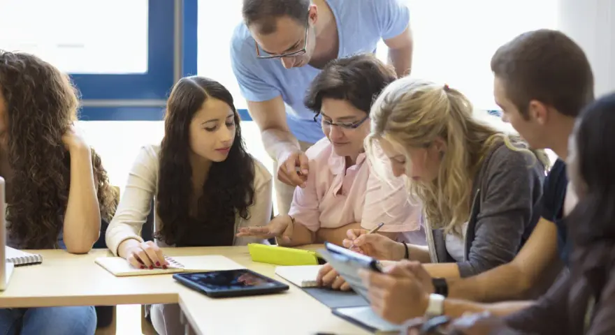 Des étudiants travaillent en groupe, un enseignant les supervise. Ils préparent leur diplôme BAFD, concentrés sur leurs notes et tablettes.