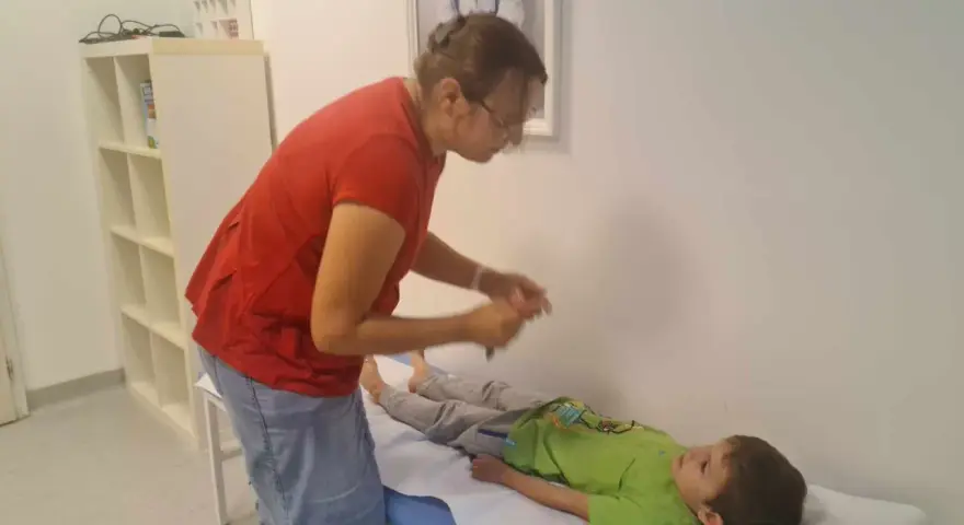 Lekarz bada chłopca leżącego na kozetce, oceniając objawy uszkodzonego układu nerwowego u dziecka.