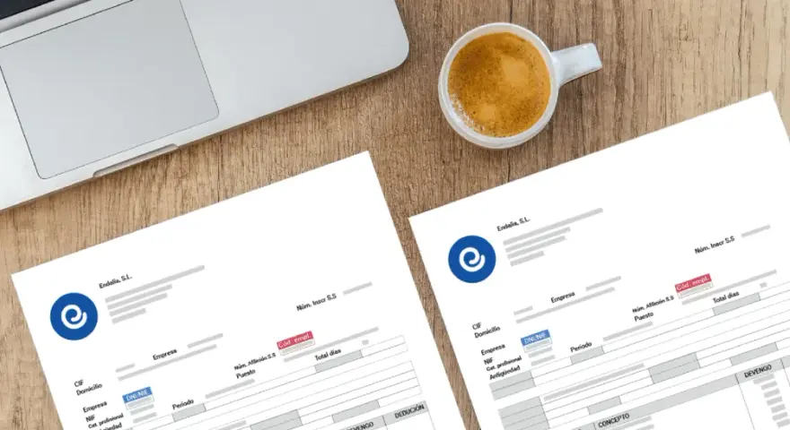 Documentos de nómina listos para ser procesados con un programa para hacer nominas. Café y portátil sugieren un entorno de trabajo.