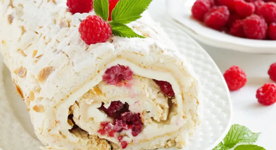 Rolada bezowa z mascarpone i malinami, posypana cukrem pudrem i płatkami migdałów.
