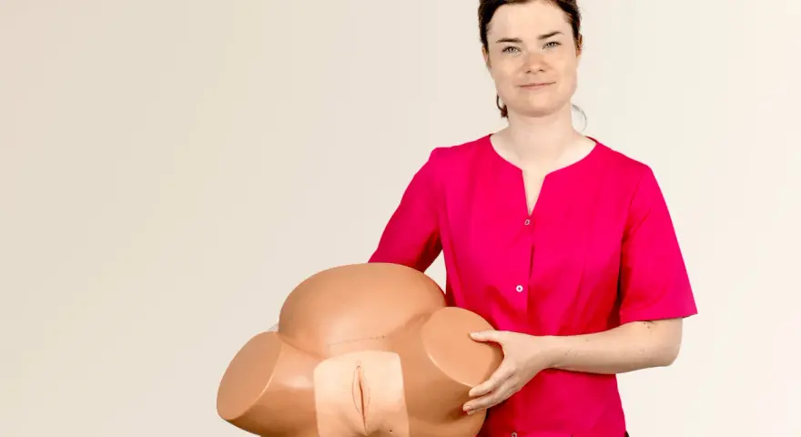 Kobieta w różowej bluzce prezentuje model miednicy do nauki masażu krocza przed porodem.