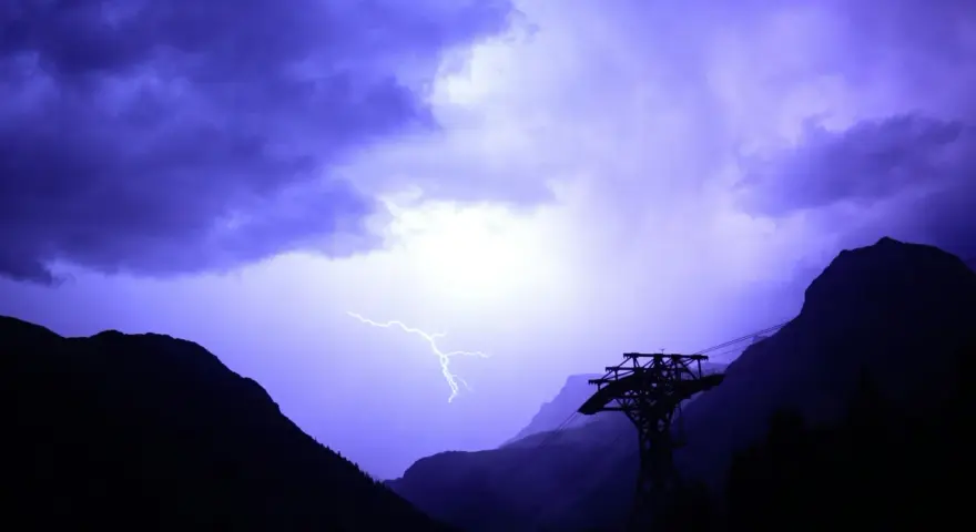Un éclair zèbre le ciel violet d'un **orage en montagne que faire** ? Une cabine de téléphérique silhouette se dresse, témoin de la fureur de la nature.