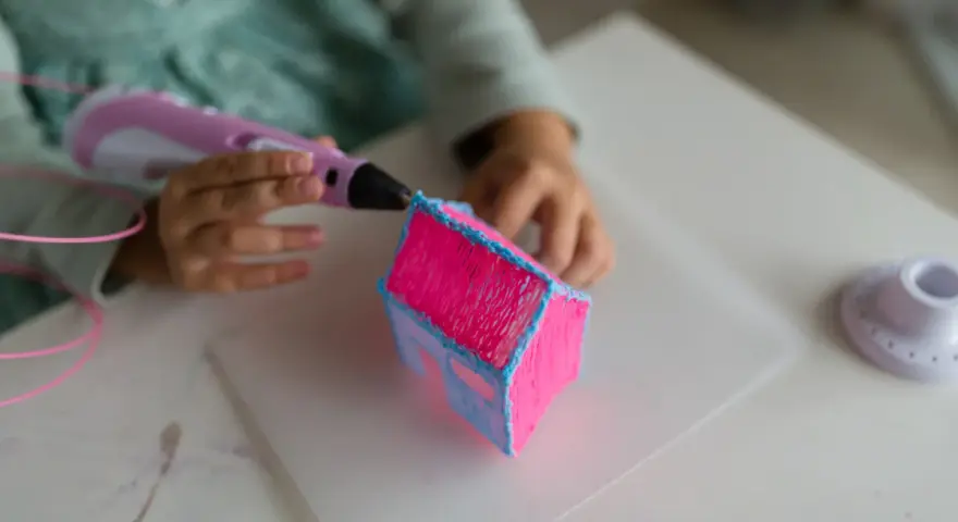 Dziecko tworzy domek z różowego i niebieskiego filamentu. Długopis 3d nie wciąga filamentu, ale tworzy trójwymiarowe dzieło.