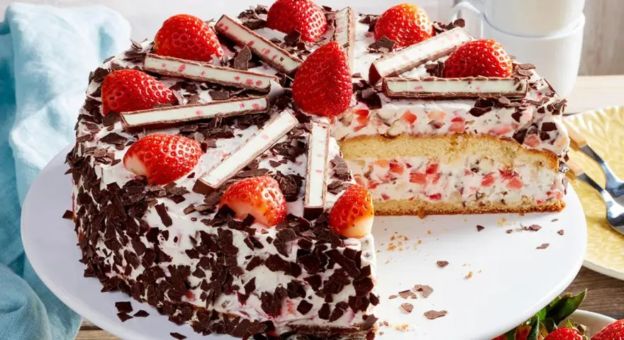 Eine köstliche Yogurette Torte mit frischen Erdbeeren, Schokostückchen und Sahne. Ein Stück ist bereits angeschnitten.