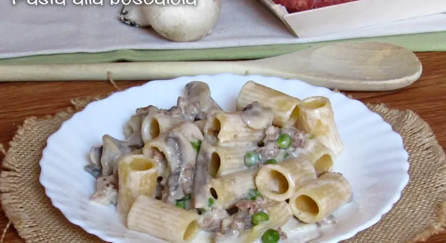 Piatto di pasta alla boscaiola con funghi, piselli e salsiccia, servita su un piatto bianco con una tovaglietta di juta.