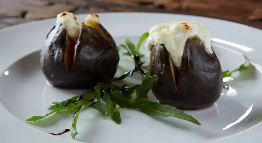 Zwei gefüllte Feigen, die auf einem Teller mit Rucola und Balsamico-Glasur liegen. Ein köstliches Gericht, das zeigt, wie man Feigen grillen kann.