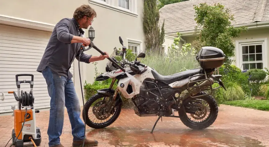 Uomo lava moto a idropulitrice in giardino. Ecco come lavare la moto a casa per mantenerla splendente.