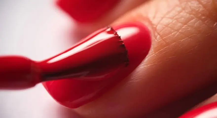 Application d'un vernis rouge vif sur un ongle. Le temps de séchage du vernis à ongles est crucial pour un fini parfait.
