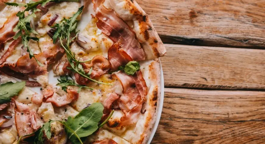 Pyszna pizza carbonara z chrupiącym boczkiem i rukolą na drewnianym stole.