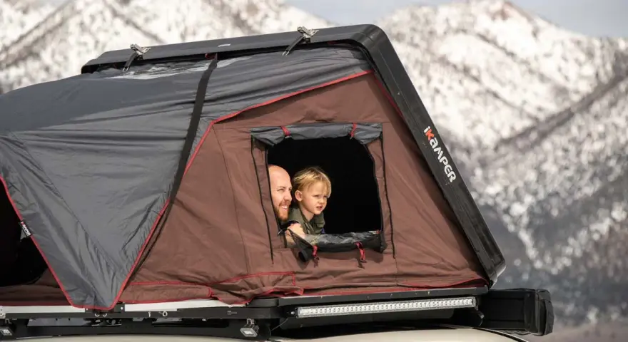 Vater und Kind schauen aus einem Dachzelt. Ein Abenteuer im Winter mit dem Dachzelt ist möglich.