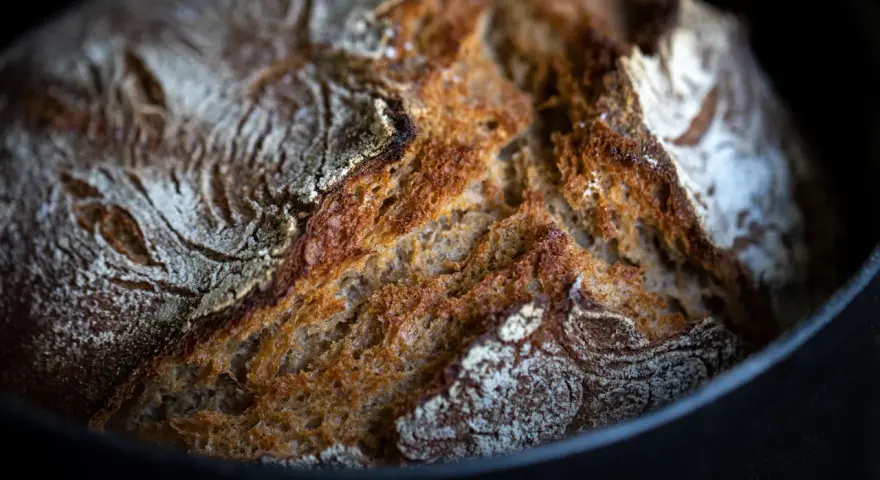 Frisch gebackenes Brot mit knuspriger Kruste ruht auf Backpapier im Gusseisentopf.