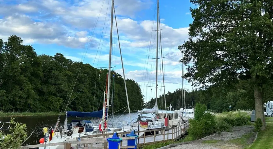 Segelbåtar vid kajen på Dalbergså camping. Grönskande träd och en blå himmel med moln.