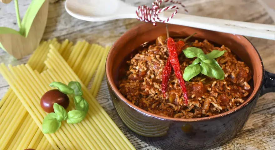 Un invitante ragù, pronto per la pasta, con peperoncini e basilico. La ricetta perfetta per un pranzo gustoso.