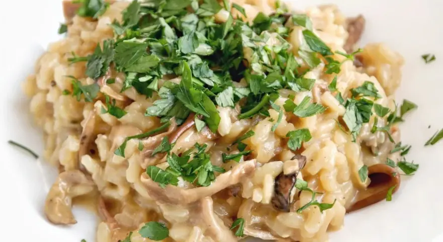 Kremowe risotto z grzybami, posypane świeżą natką pietruszki, wygląda apetycznie.