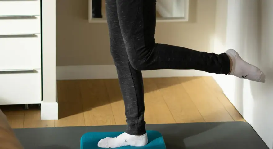 Personne effectuant des exercices de renforcement de la cheville sur un step bleu, idéal pour la rééducation après une entorse.