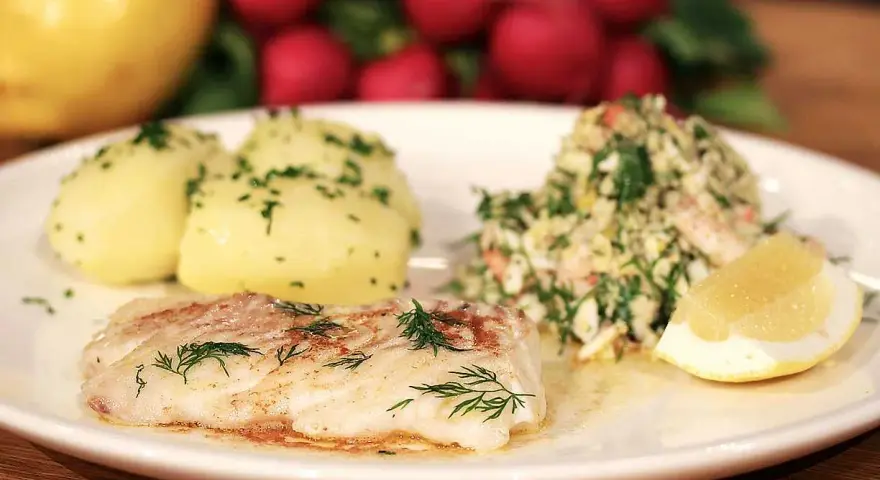 En tallrik med stekt kolja, dill, potatis och en citronskiva. Ett perfekt kolja recept för en god middag.