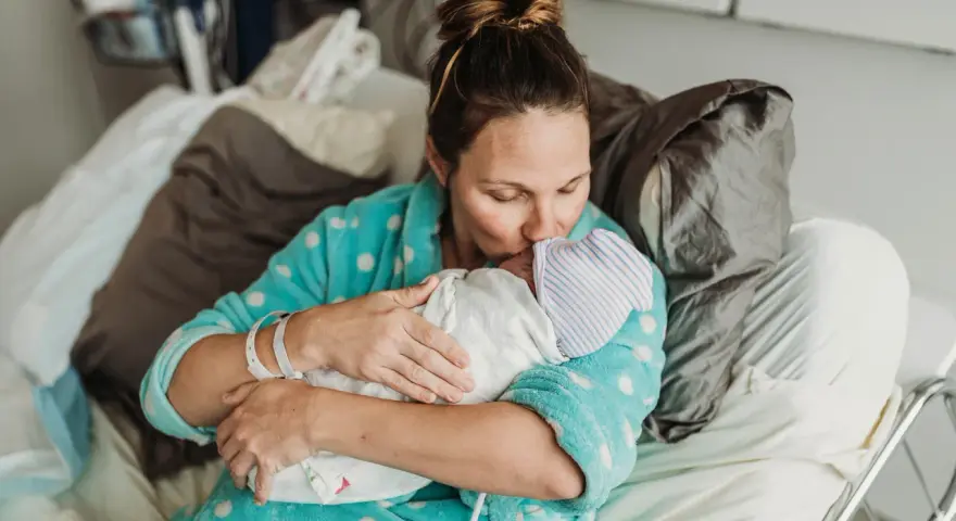 Mama tuli dziecko po cesarce, czule całując je w czapeczkę. Laktacja po cesarce może być wyzwaniem, ale miłość jest silniejsza.