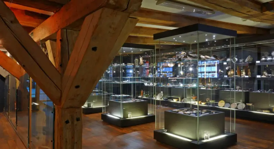 Wnętrze muzeum z zabytkowymi belkami i przeszklonymi gablotami pełnymi artefaktów. Może tu jest też błękitny baranek?
