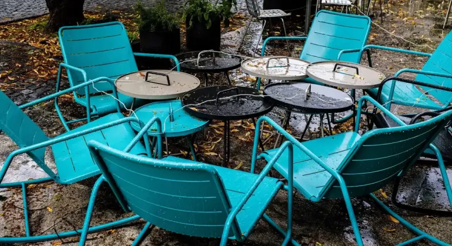 Teal metal chairs and tables, perfect for outdoor use, sit empty on a wet patio.