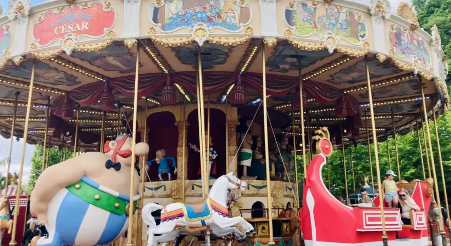 Karuzela z postaciami z komiksów Asterixa w parku rozrywki. Obok Obelixa, biały koń i czerwony statek wikingów.