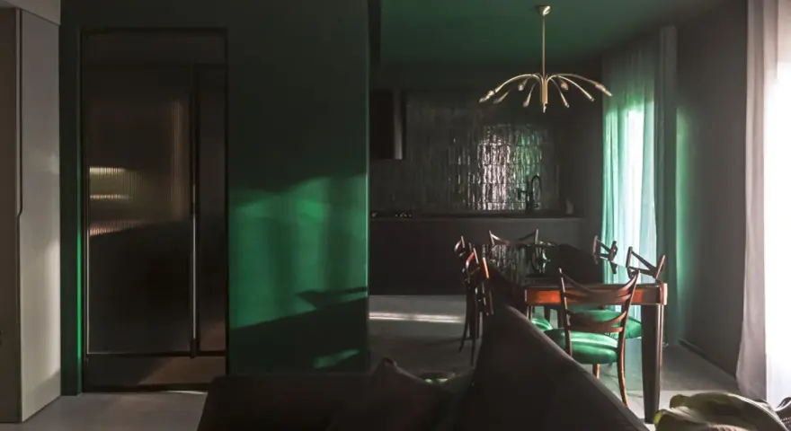Un soggiorno moderno con pareti verde scuro, un divano antracite e una zona pranzo con sedie verdi. I colori da abbinare al verde scuro sono il legno scuro e l'ottone.