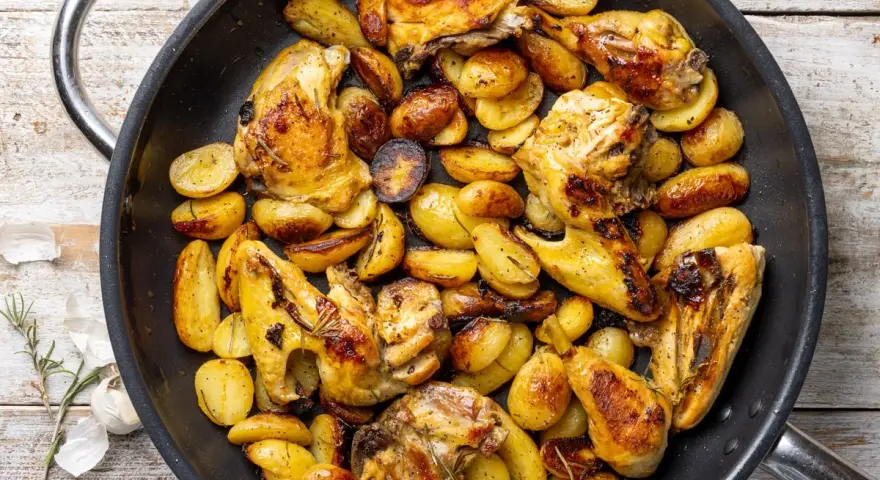 Pollo con patate in padella, dorato e saporito, con erbe aromatiche. Un piatto rustico e invitante.