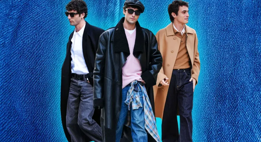 Tre uomini con un outfit elegante con jeans. Uno indossa un cappotto nero, camicia bianca e jeans grigi. Un altro un cappotto in pelle nero, maglione rosa e jeans blu. Il terzo un cappotto cammello, maglione marrone e jeans scuri.