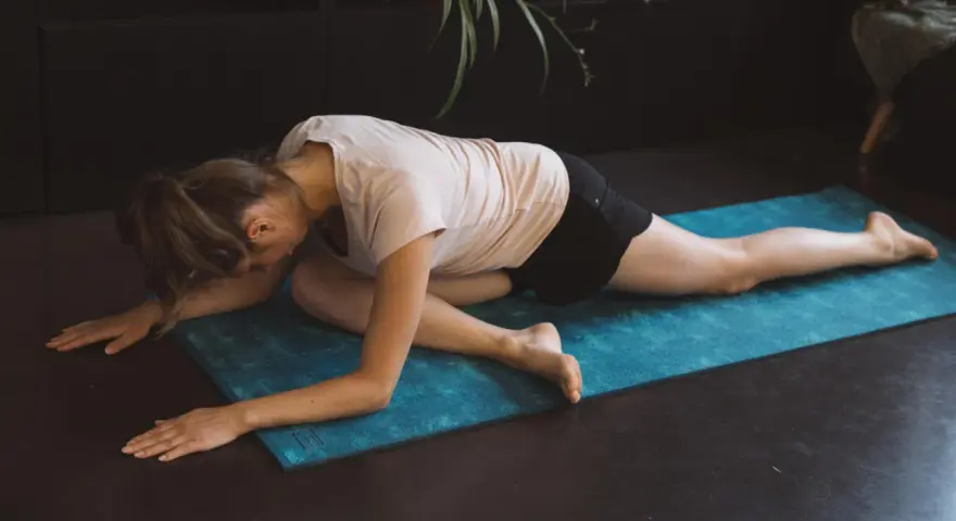 Femme en posture de pigeon sur un tapis bleu, un excellent exercice pour le dos à la maison.