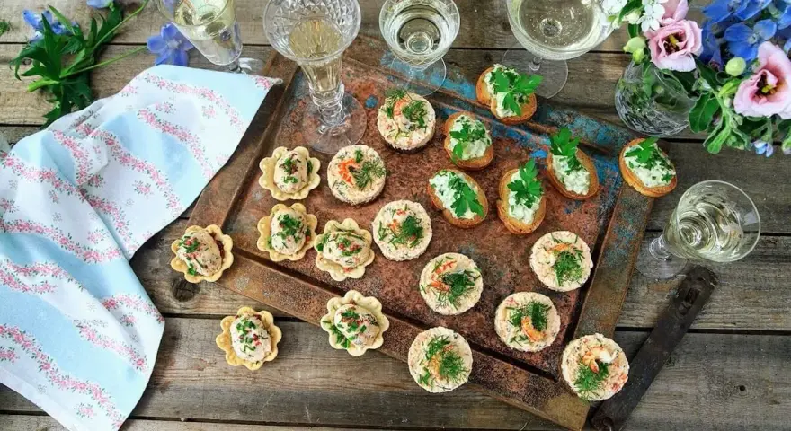 Små, läckra tilltugg till bubbel, serverade på en rustik bricka med blommor och glas. Perfekt för festliga tillfällen.
