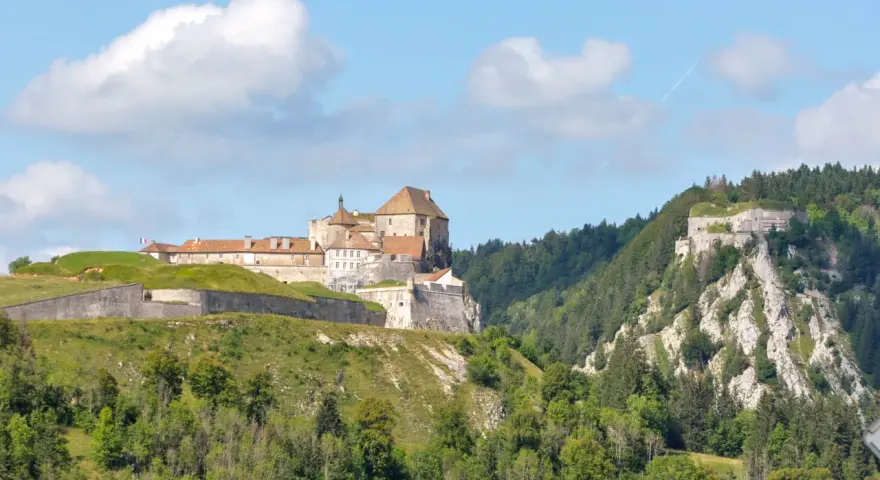 Fort de Joux, un site historique à visiter dans le Doubs, perché sur une colline verdoyante sous un ciel bleu.