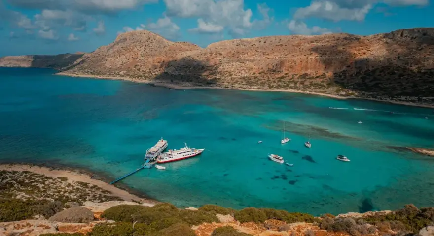 Wycieczka na Santorini z Krety: statki cumują w turkusowej zatoce, otoczonej skalistymi wzgórzami.