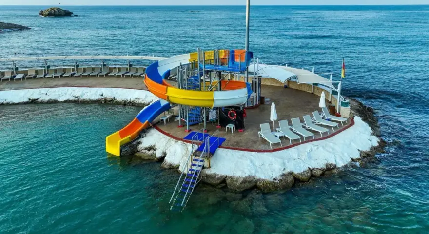 Kolorowe zjeżdżalnie wodne i leżaki na wyspie w Orange County Alanya, nad turkusowym morzem.