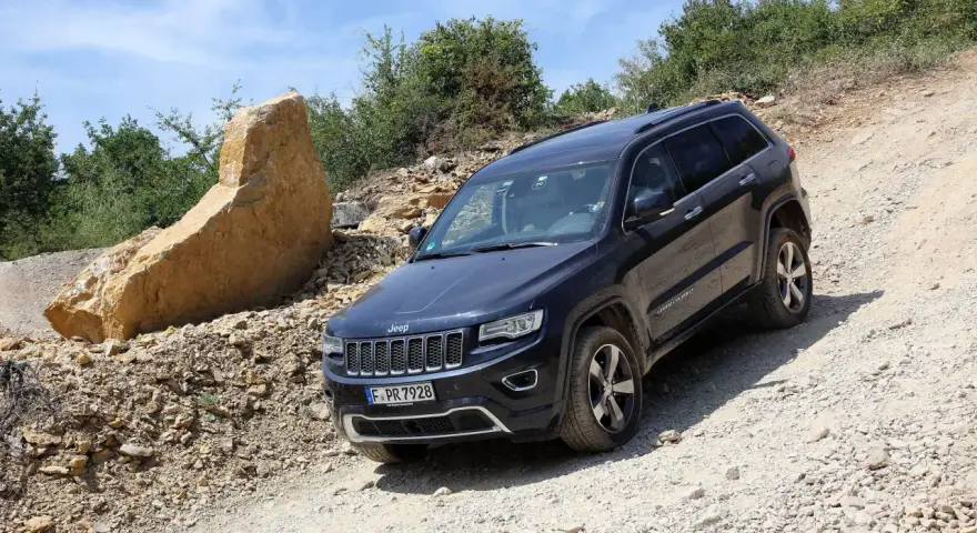 Schwarzer Jeep Grand Cherokee 3.0 CRD 250 PS im Gelände. Ein großer Felsbrocken liegt daneben.