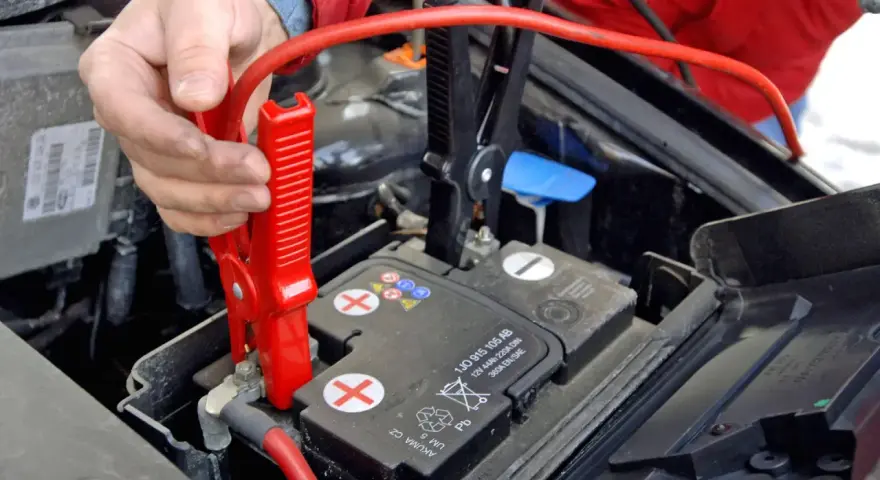 Hand befestigt rote Klemme an Autobatterie. Die richtige **Starthilfe Reihenfolge** ist entscheidend für die Sicherheit.
