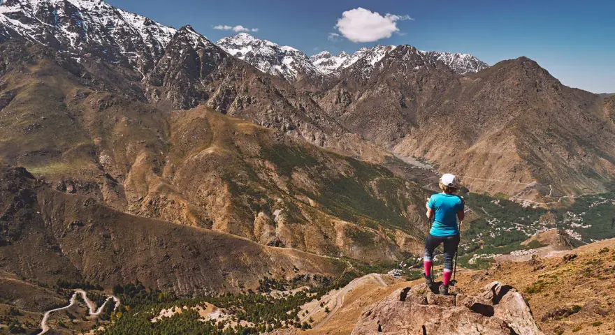 Widok na ośnieżone szczyty górskie Jebel Toubkal. Turystka podziwia panoramę z skalistego zbocza.