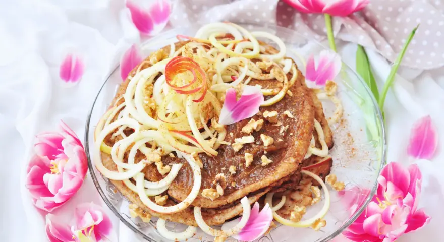 En vacker pannkakstårta med äpple, kanel och valnötter, perfekt för ett pannkakstårta recept. Omgiven av rosa tulpaner.