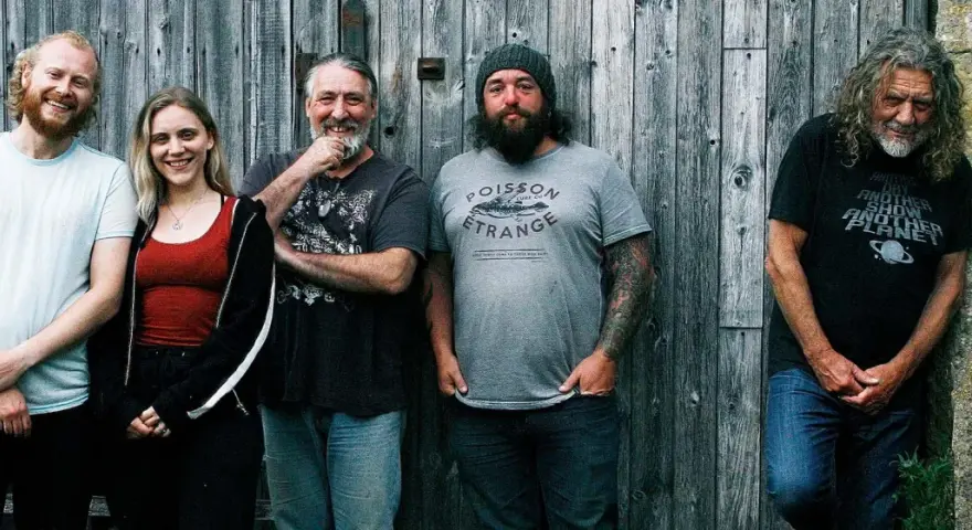 Le groupe de Robert Plant, avec ses musiciens, pose devant un mur de bois.