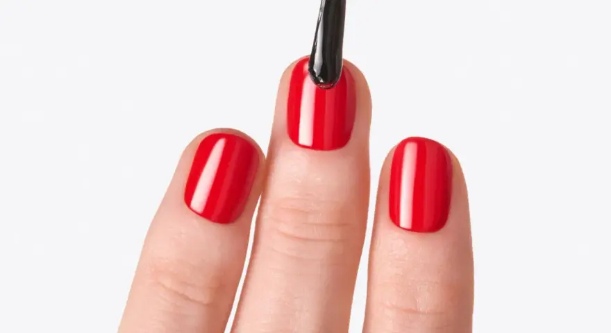 Application d'un top coat sur des ongles rouges brillants. Le top coat, c'est quoi ? C'est la touche finale pour une manucure parfaite.