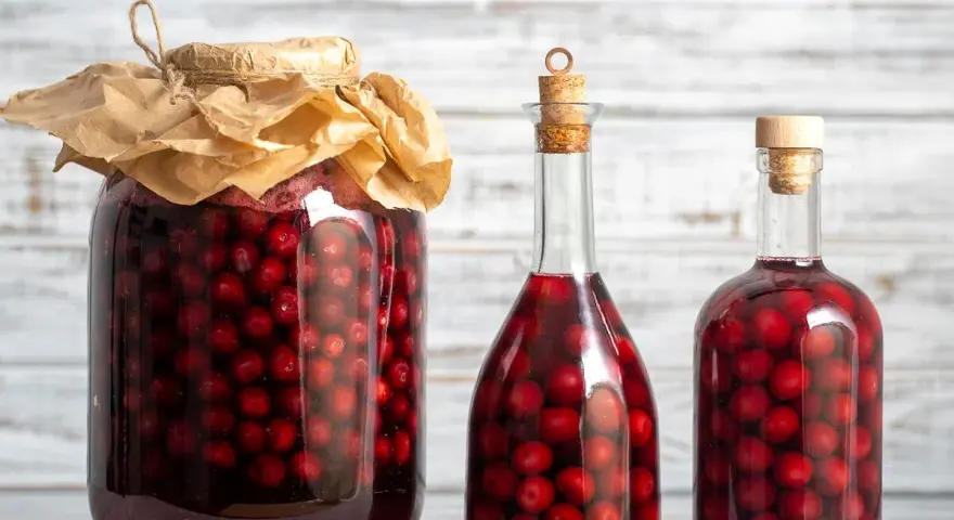 Ein großes Glas und zwei Flaschen gefüllt mit Kirschen und Alkohol. Perfekt für ein schnaps selber machen rezept.
