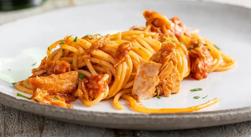 Spaghetti al tonno conditi con un sugo saporito e ricchi pezzi di tonno, guarniti con prezzemolo fresco.