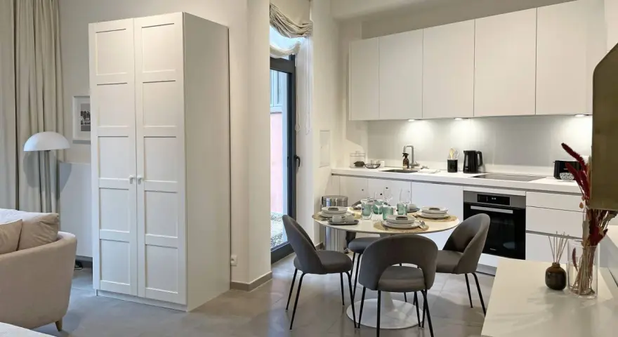 Acogedor cocina salón comedor de 30 m2 con muebles blancos, mesa redonda y sofá.