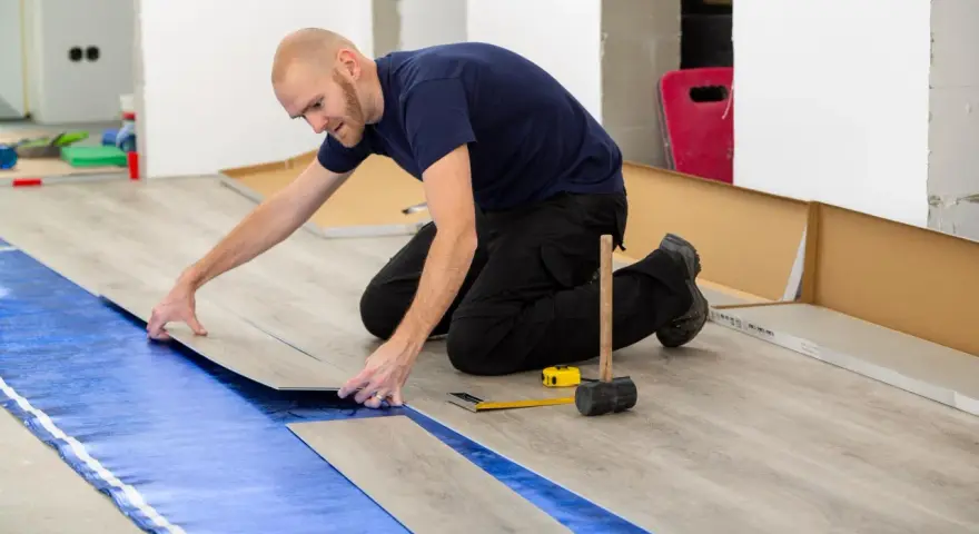 Pose d'un revêtement de sol stratifié sur une sous-couche d'isolation phonique sous carrelage. Outils de pose à proximité.