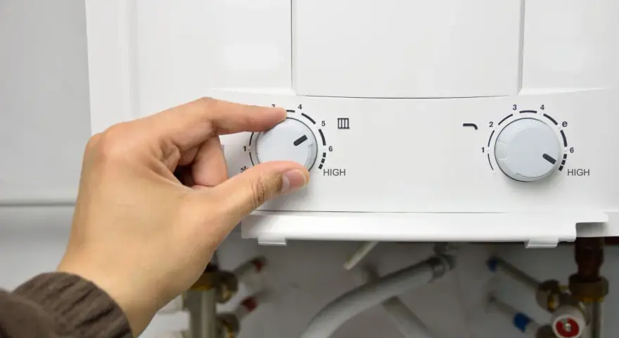 Mano girando el dial del termo eléctrico para cerrar la llave de paso.