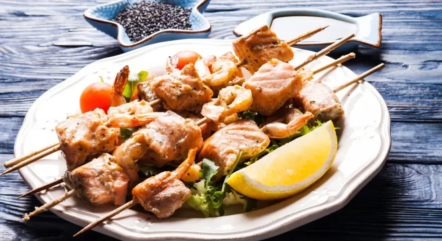 Spiedini di pesce succulenti, con gamberi e salmone grigliato, serviti su un letto di insalata con spicchio di limone.