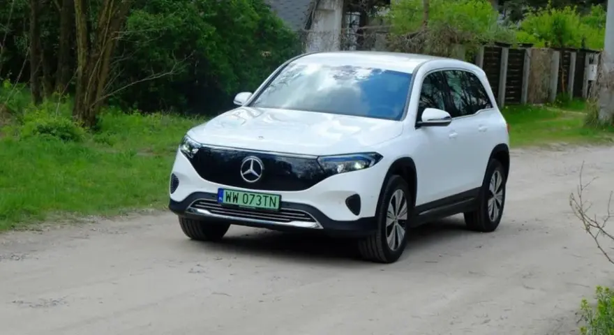 Biały Mercedes EQB na drodze gruntowej, otoczony zielenią.