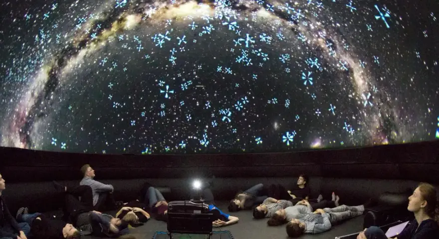 Besucher im Planetarium Berlin liegen und sitzen und blicken gebannt auf die Projektion der Milchstraße und funkelnder Sterne.